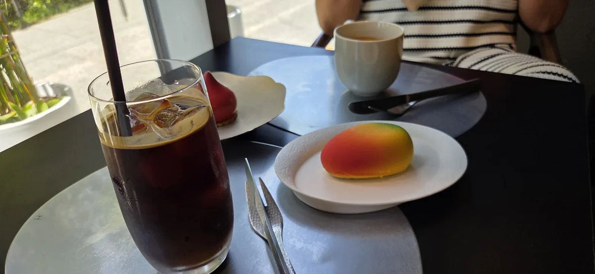 Table setting with gradient-colored pastry, dark beverage, and ceramic mug in bright cafe.