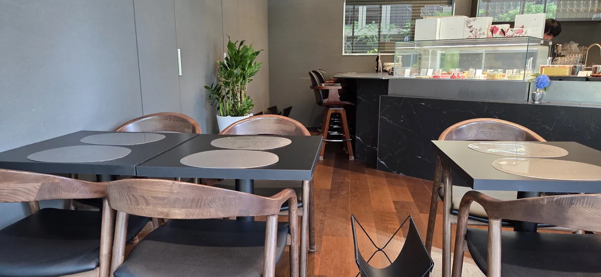 Modern dining space with dark tables, wooden chairs, and a black marble counter serving area.