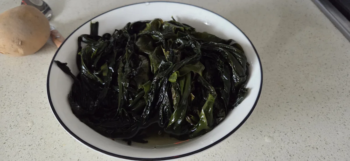 Cooked dark seaweed strips in a white bowl with blue rim on countertop.