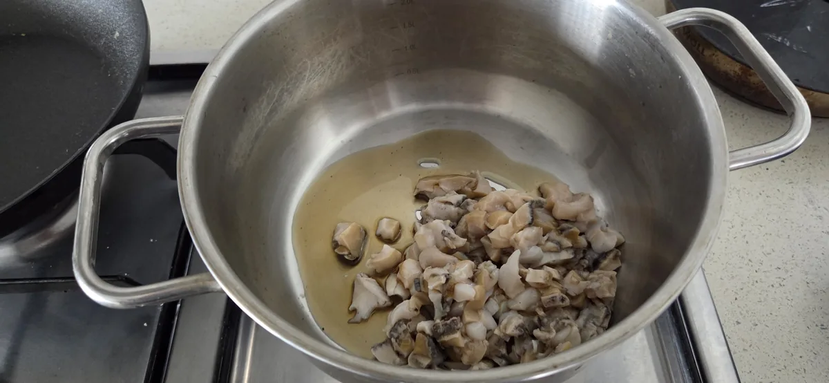 Chopped abalone pieces rest in a light broth inside a stainless steel pot on a stovetop.