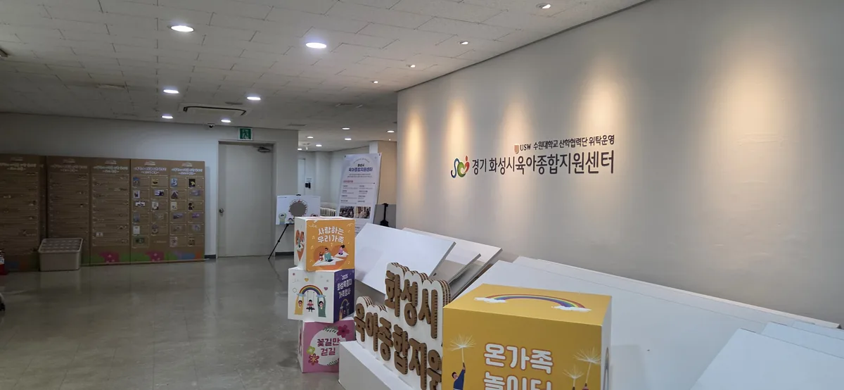 Lobby of the Gyeonggi Hwaseong Childcare Support Center, with its wall sign and stacked cardboard display cubes reading 화성시 육아종합지원센터.