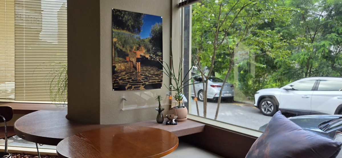 Window seating at Fullmoon cafe with round wooden tables, a rooftop-garden print on the wall and trees and parked cars outside the big window.