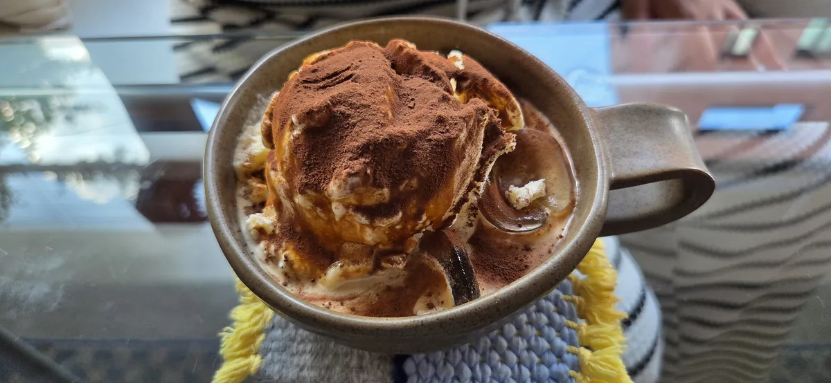 Brown stoneware mug filled with a cocoa-dusted, caramel-drizzled cream dessert at Fullmoon cafe.